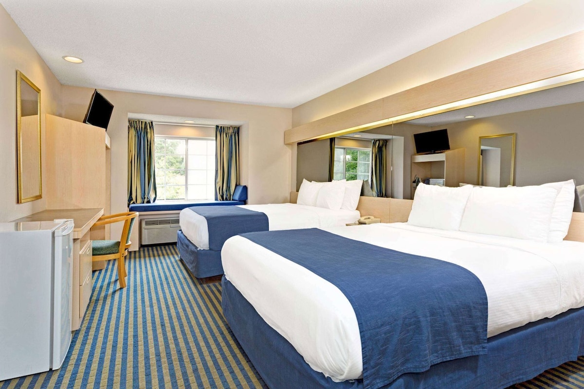 A hotel room with two beds, a desk, a chair, a TV, and a window with curtains.