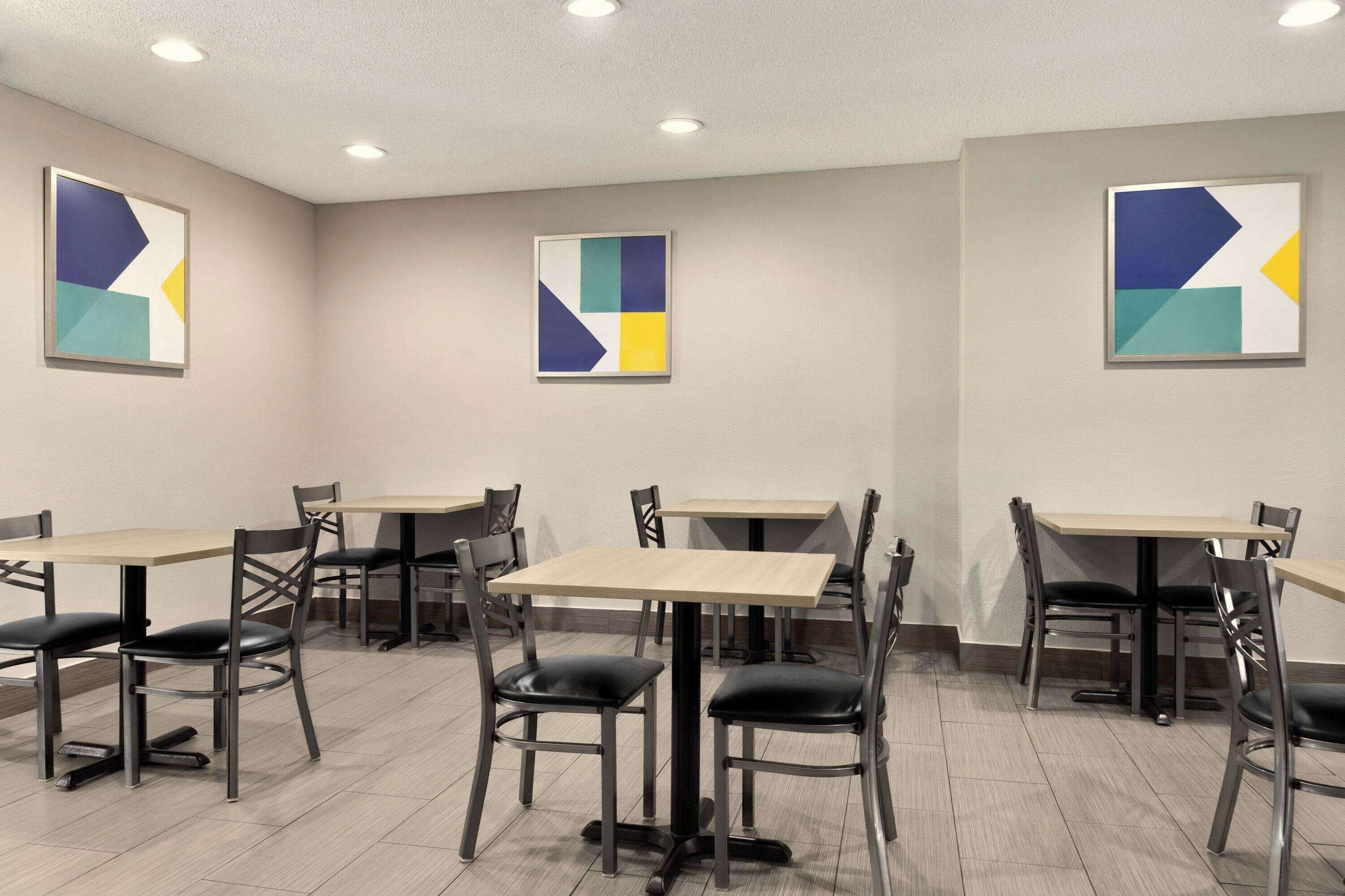 A dining area with multiple tables and chairs, geometric wall art, and recessed ceiling lighting.