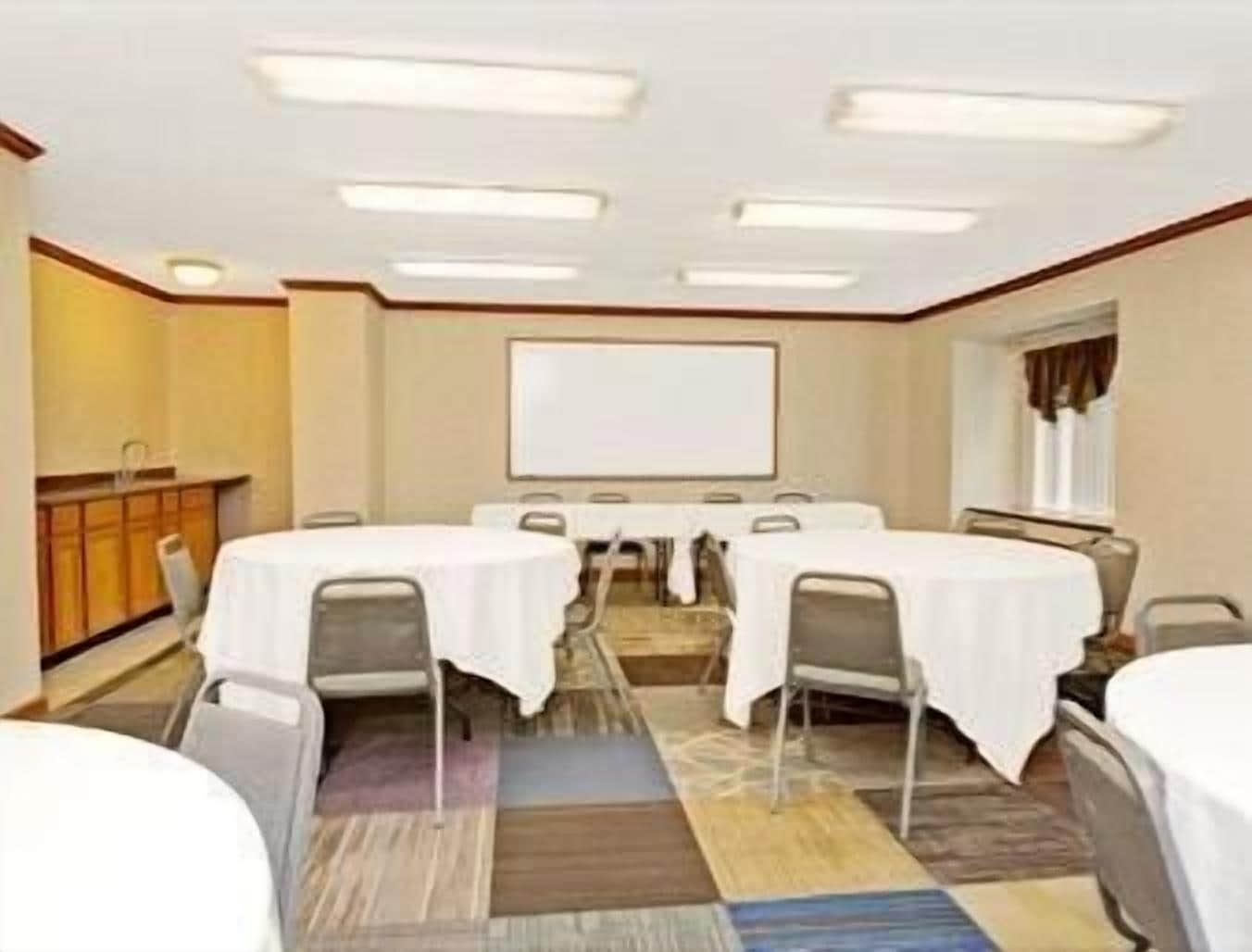 A conference room with round tables, chairs, a whiteboard, and a carpeted floor.
