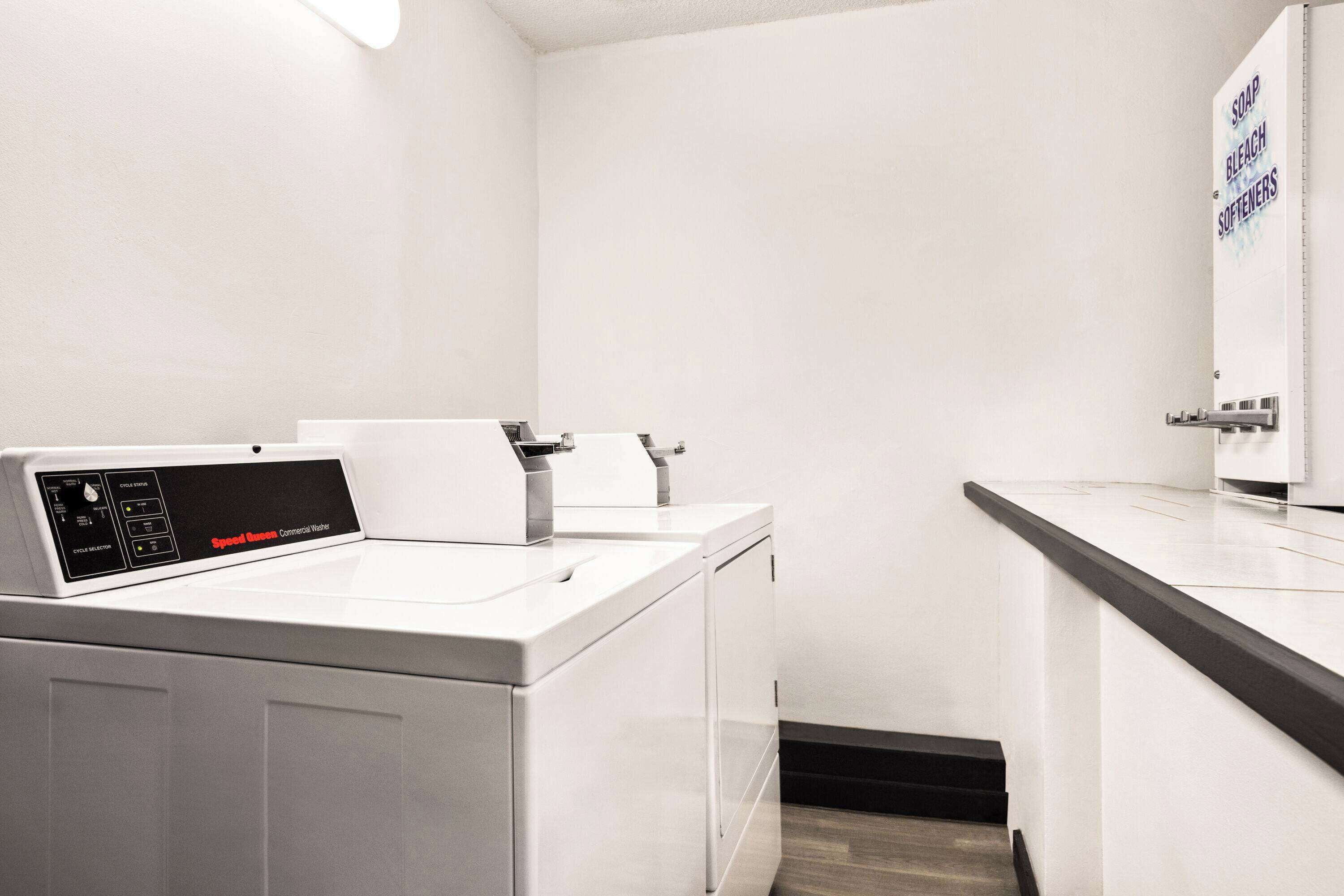 Une buanderie moderne équipée d’un lave-linge et d’un sèche-linge à chargement frontal, d’un évier et d’un distributeur de savon fixé au mur.