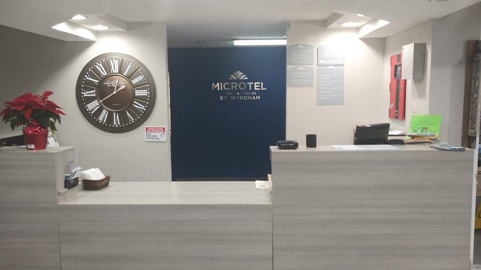 Una recepción con un reloj, un letrero que dice 'MICROTEL INN & SUITES BY WYNDHAM' y una planta en maceta.