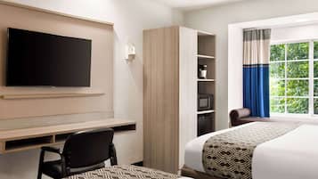 Habitación de hotel con televisión de pantalla plana, escritorio, dos camas, armario, silla y ventana con cortinas.