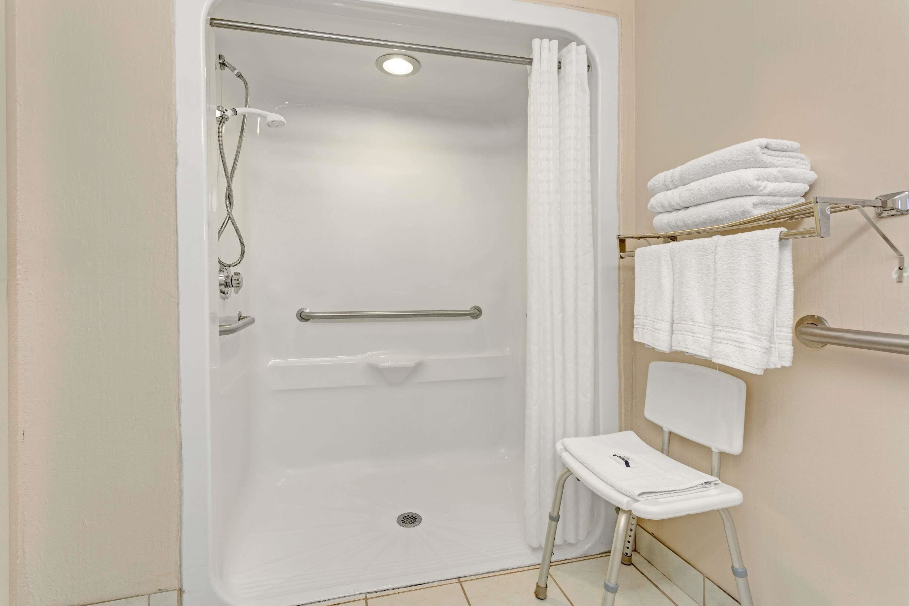 A walk-in shower with a grab bar, a white towel rack, and a white chair.