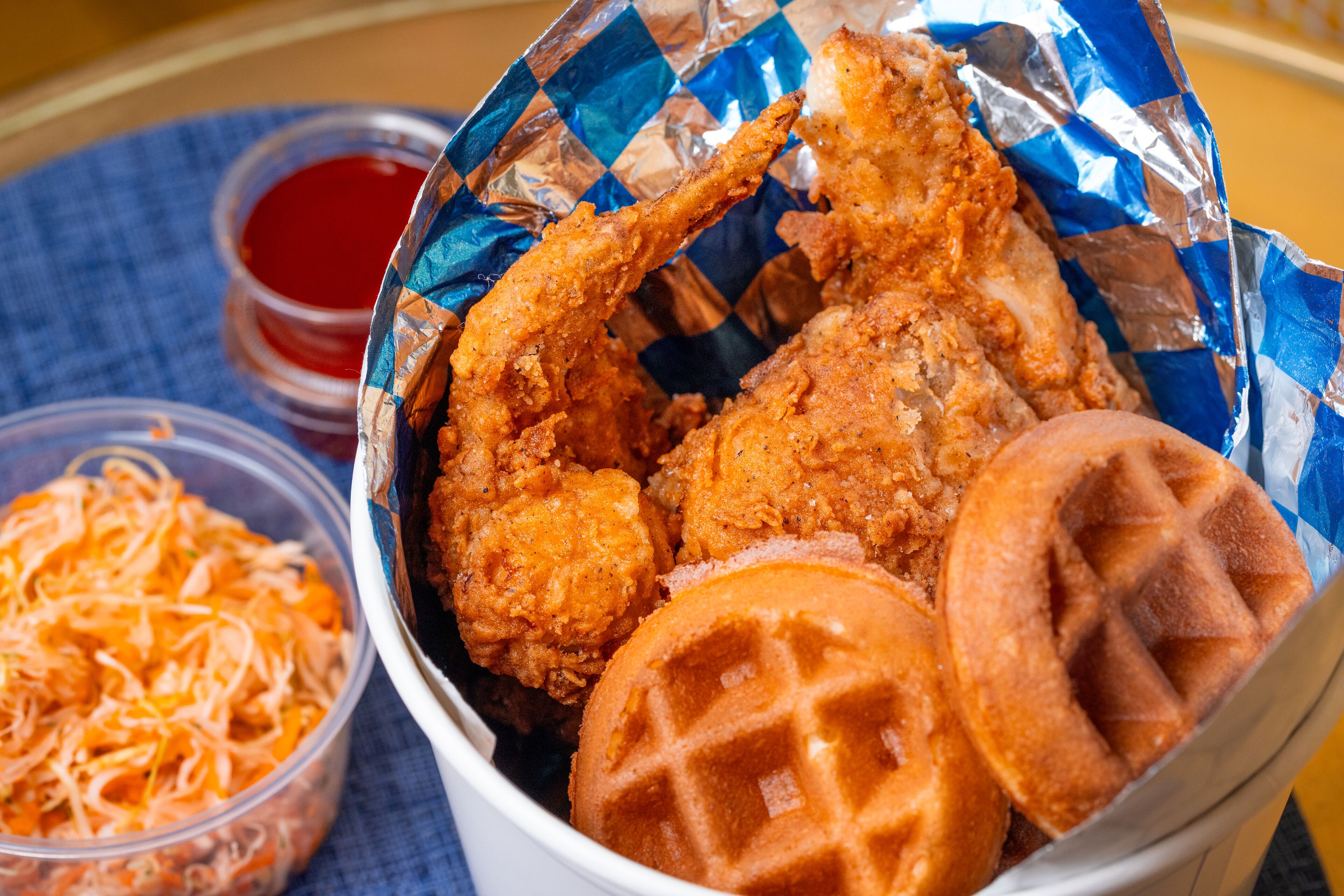 A basket containing fried chicken, waffles, and a side of shredded cheese.