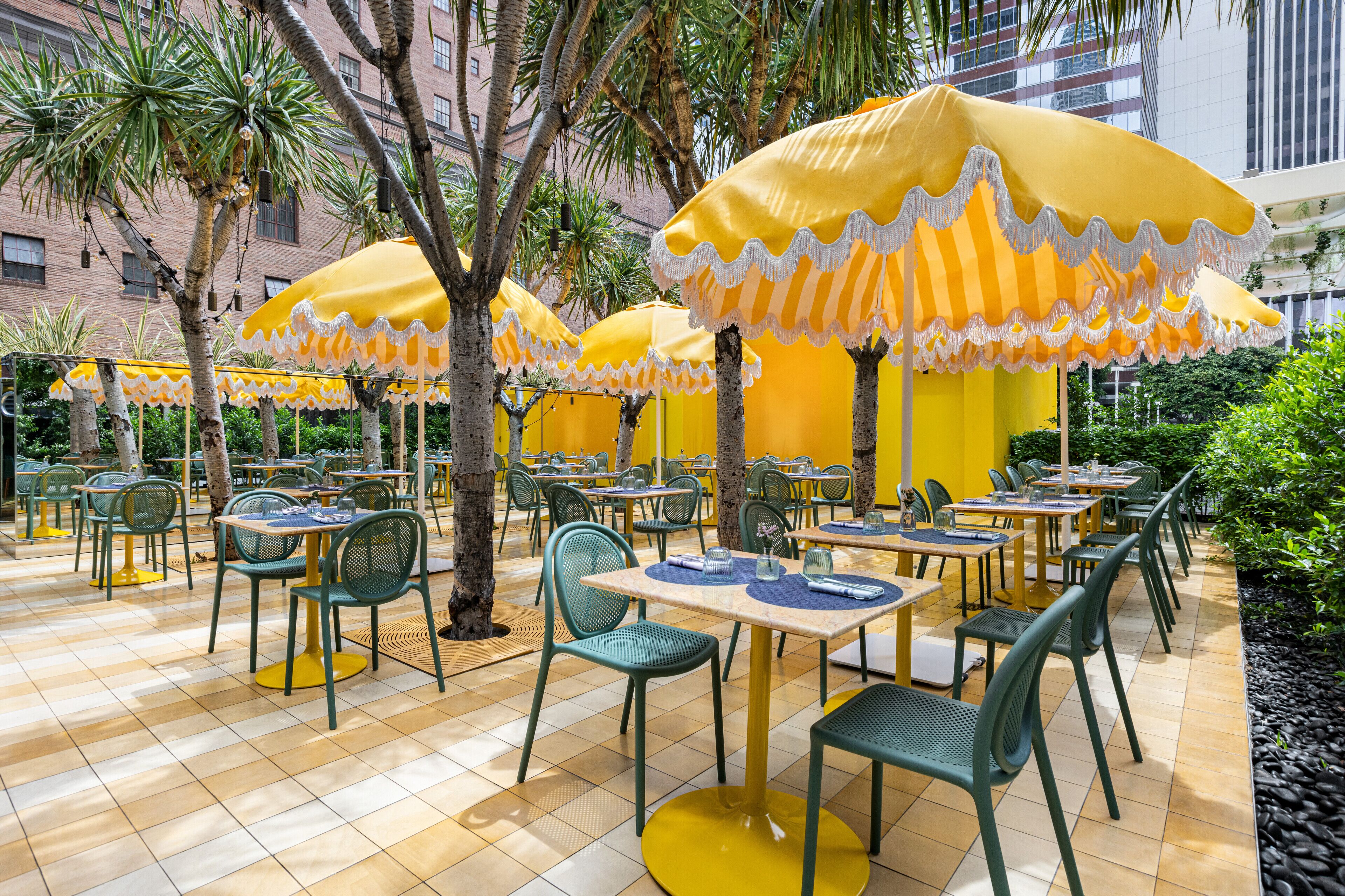 An outdoor dining area with yellow-striped umbrellas, green chairs, and tiled flooring.