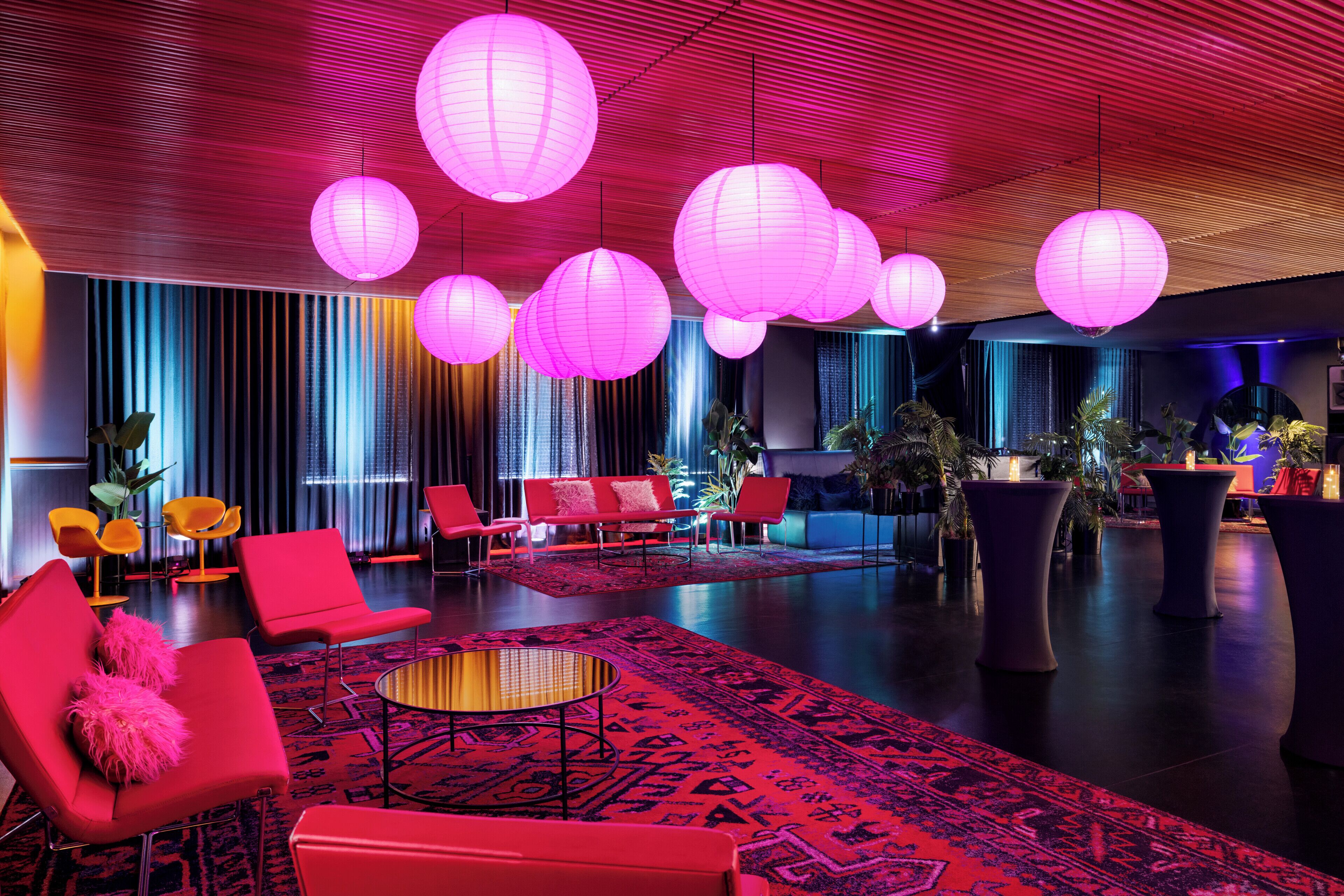 A modern lounge area with red and pink seating, large round tables, and decorative paper lanterns.