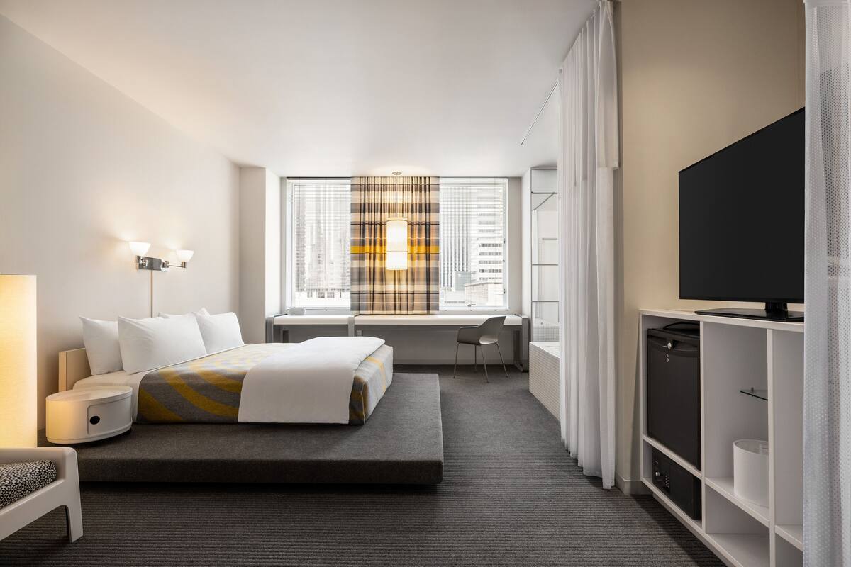 A hotel room with a bed, a desk, a chair, a TV, and a wardrobe.