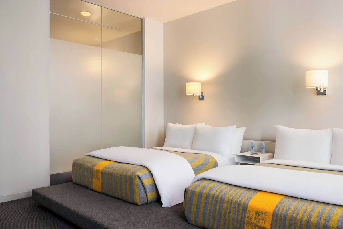 A hotel room with two beds, a small bedside table, and a mirror.