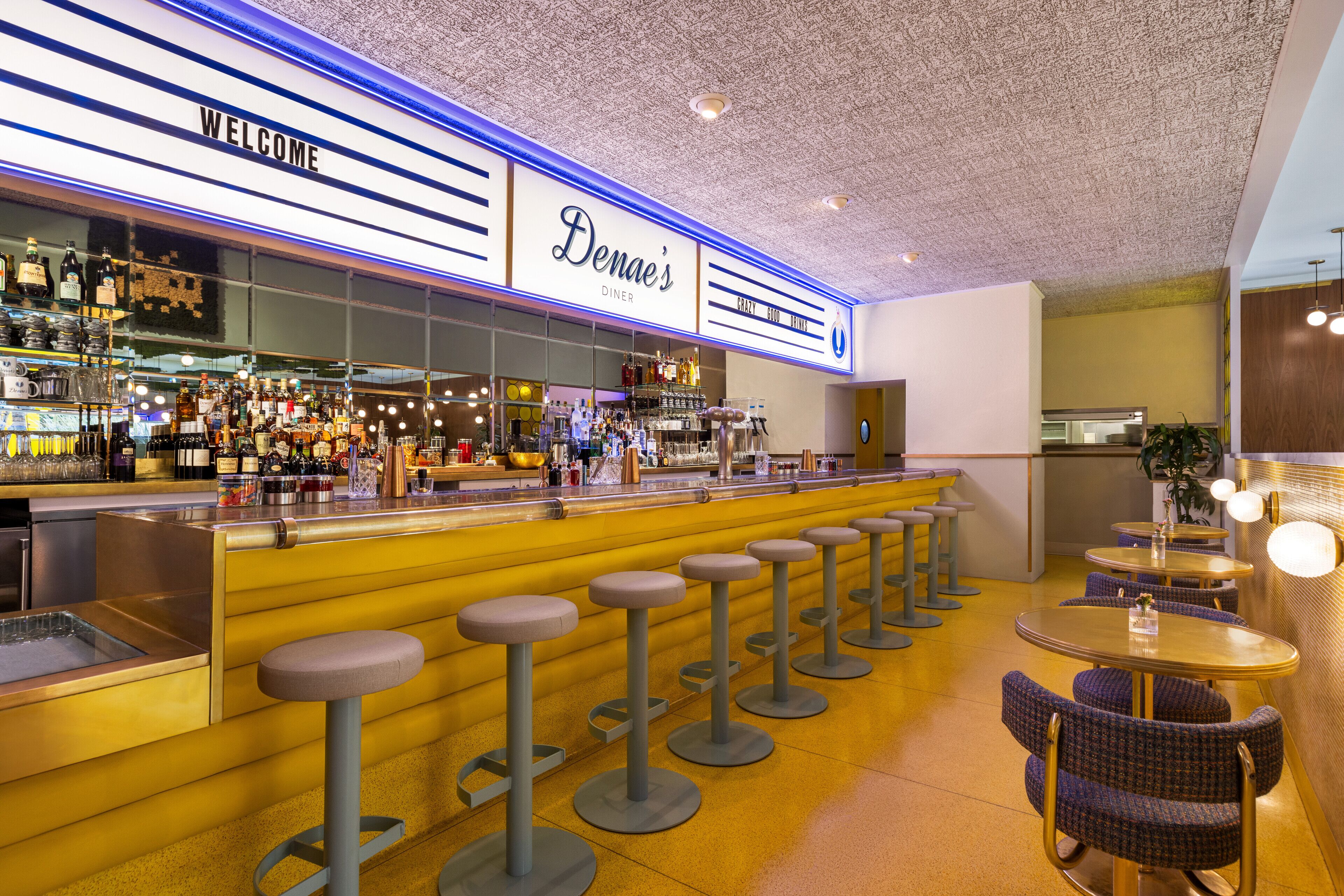 Un área de bar con taburetes, una barra con botellas y un letrero que dice "Denae's Diner".
