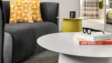 Un salón moderno con un sofá gris, almohadas amarillas y blancas estampadas, una mesa de centro blanca y libros, incluyendo 'The Art of Home' y 'Johnny Cash'.