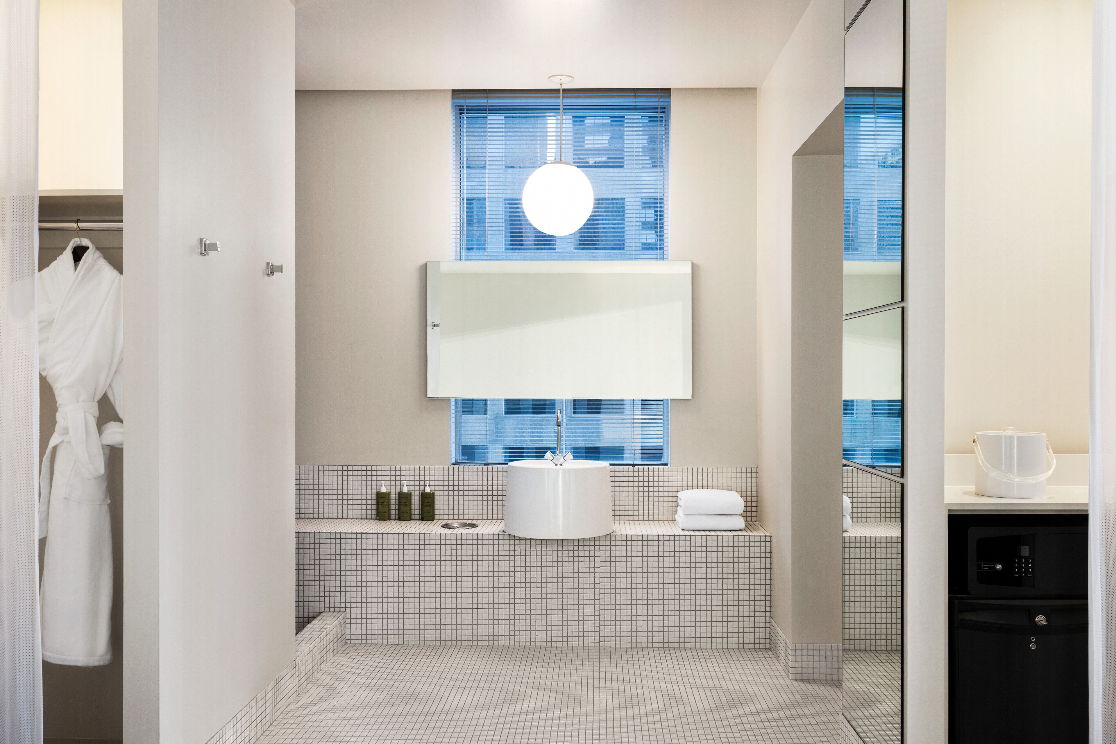 A modern bathroom with a white sink, a mirror above it, and a window with blinds.