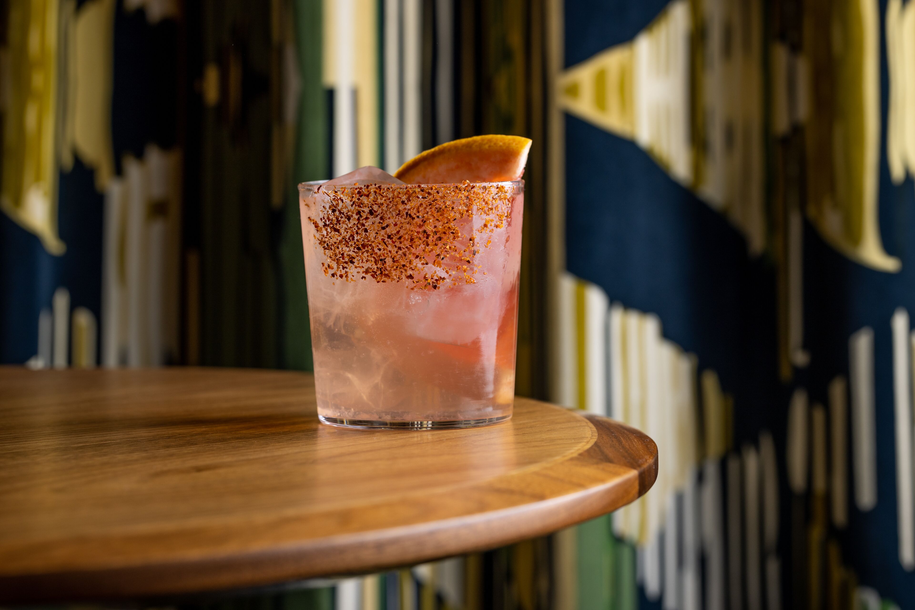 A glass of iced beverage with a garnish on a wooden table.