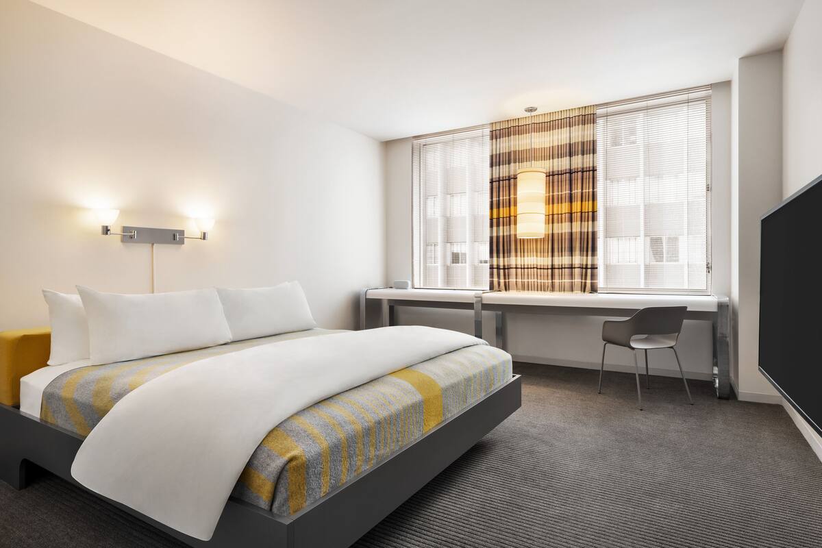 A modern hotel room with a bed, a desk, and a TV.