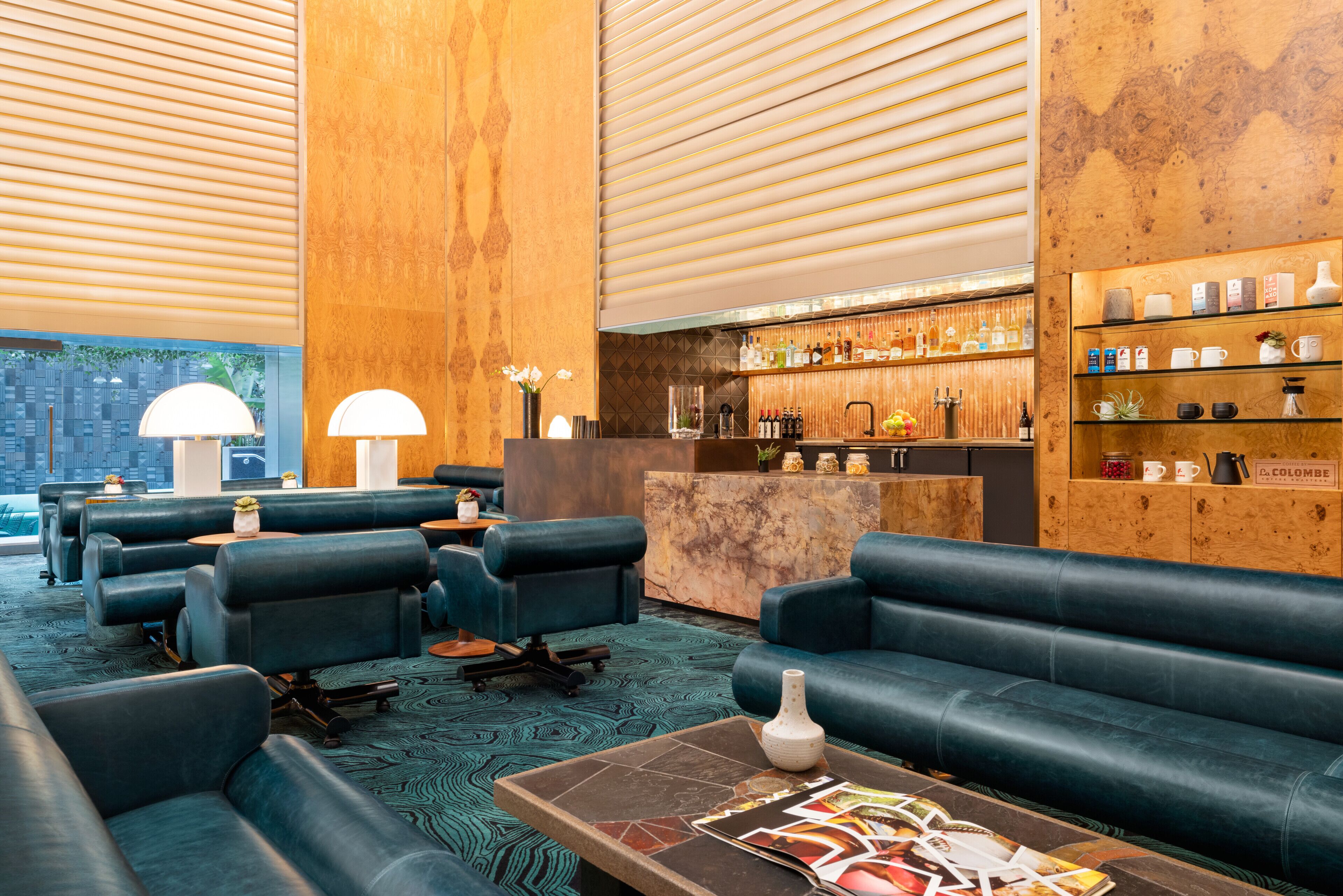 A modern lounge area with leather sofas, a coffee table with magazines, a bar with various bottles, and a wooden accent wall.