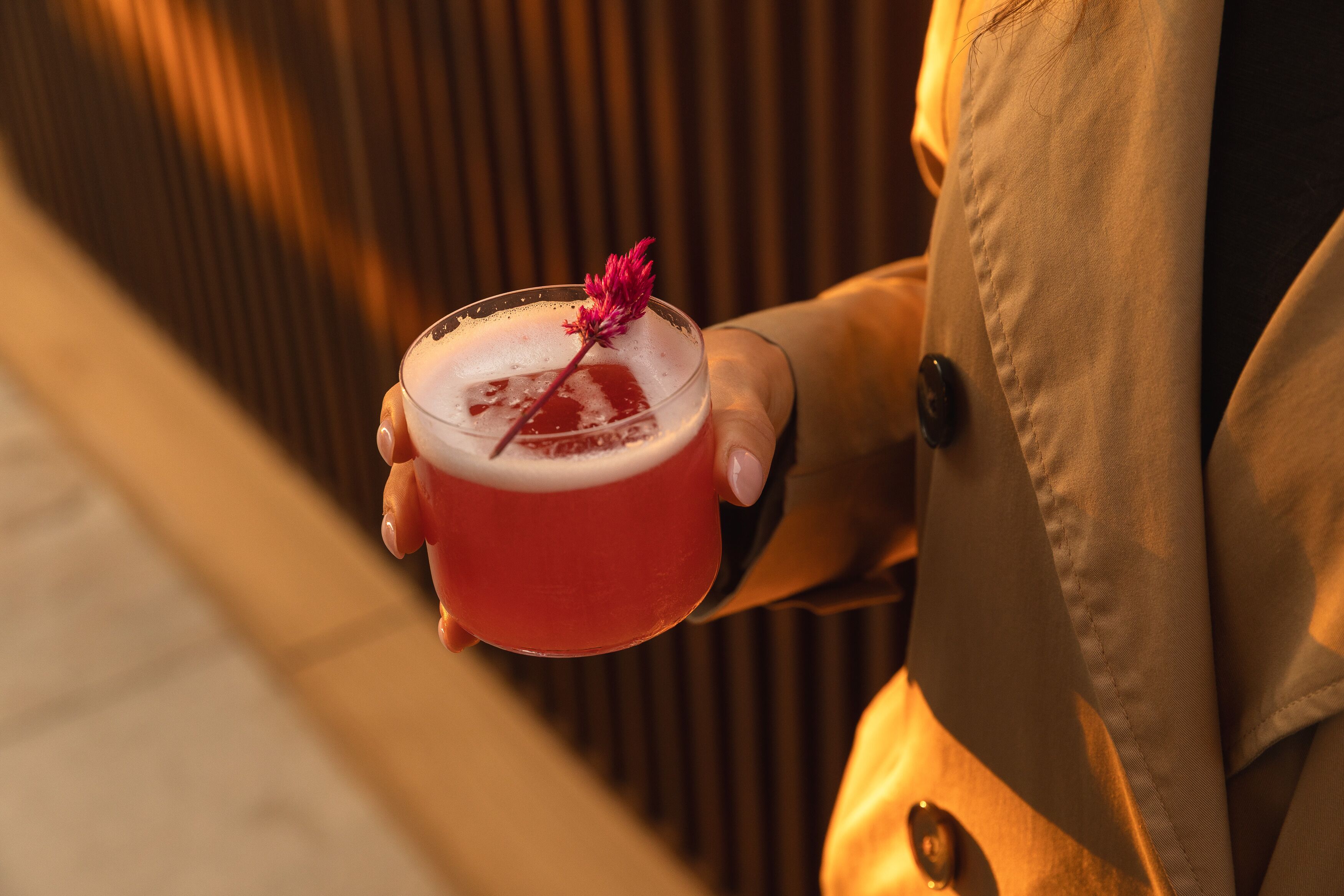 A person holding a red mug with a flower garnish.