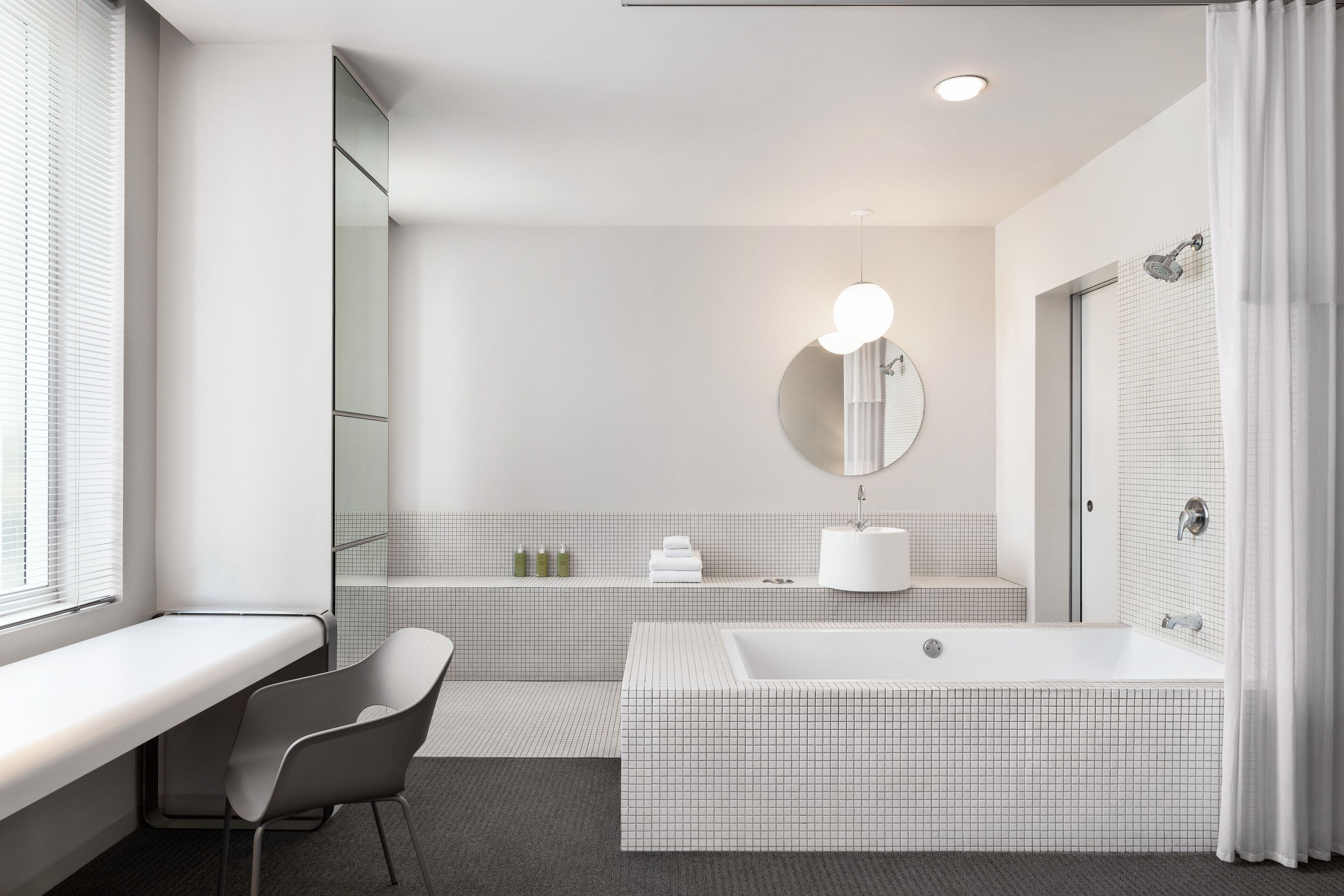 A modern bathroom with a large bathtub, a vanity with a mirror, and a window with blinds.