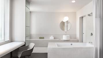A modern bathroom with a large bathtub, a vanity with a mirror, and a window with blinds.