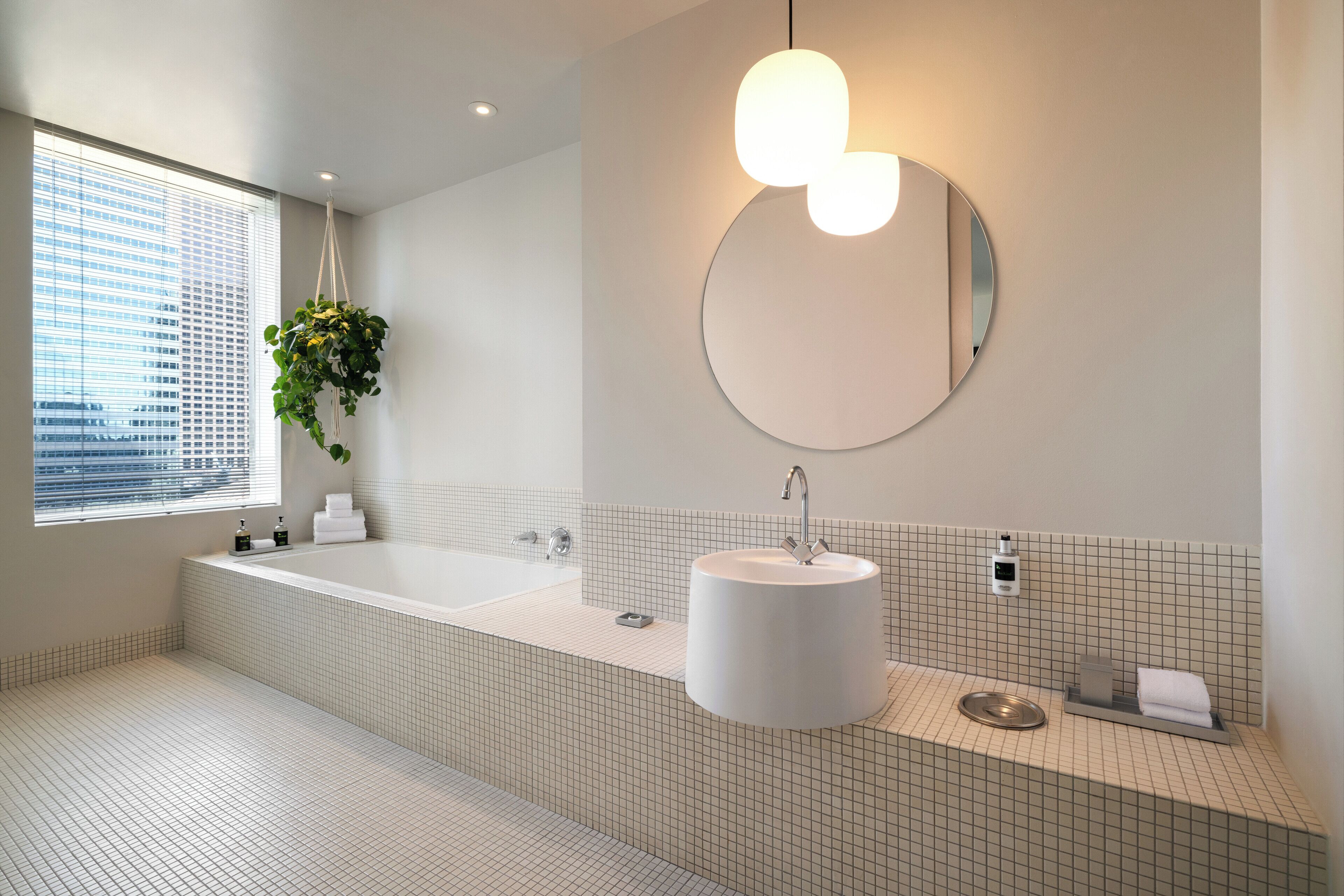 A modern bathroom with a large bathtub, a round mirror, and a sink.