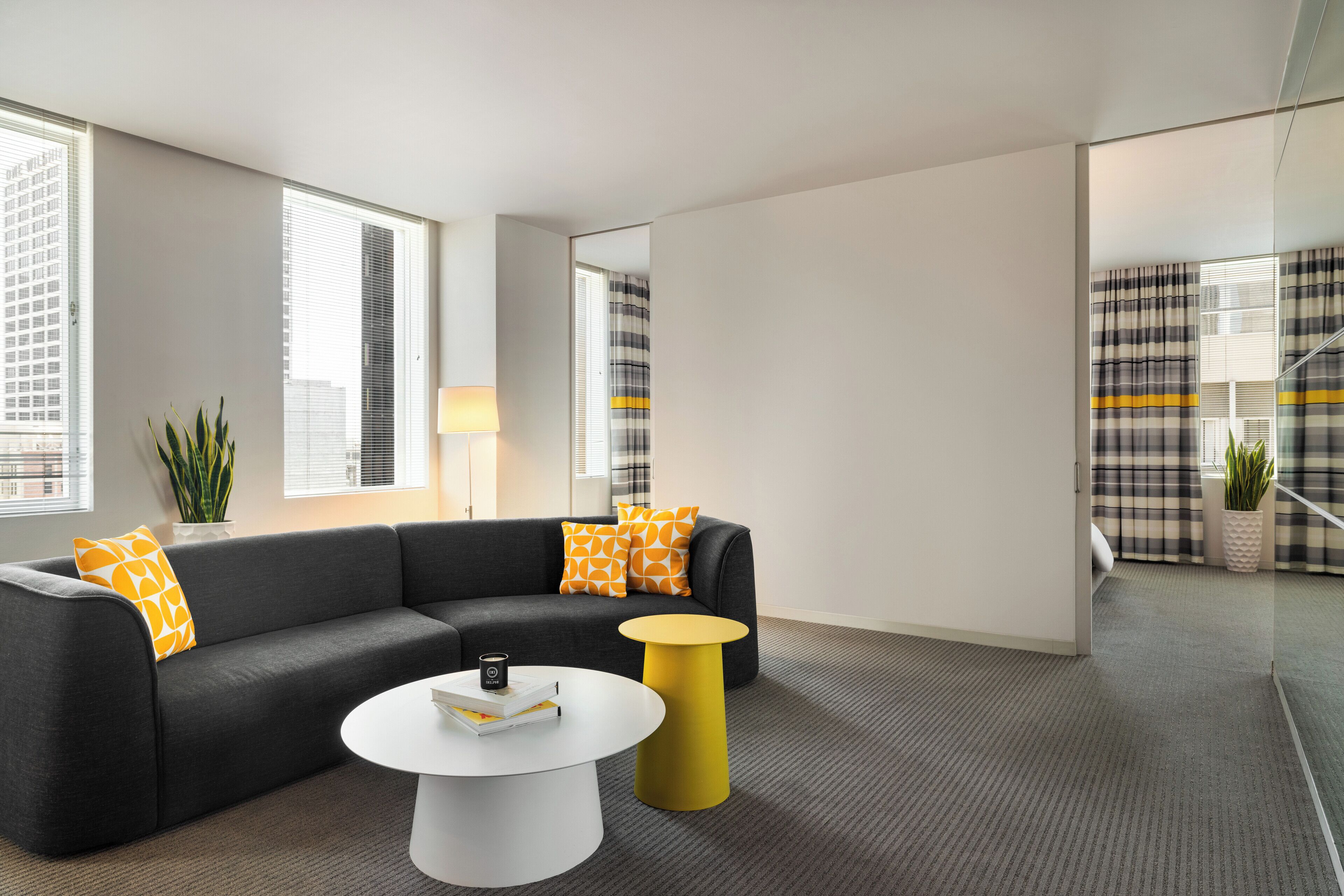 A modern living room with a grey sofa, yellow and orange pillows, a white coffee table, and a yellow side table.