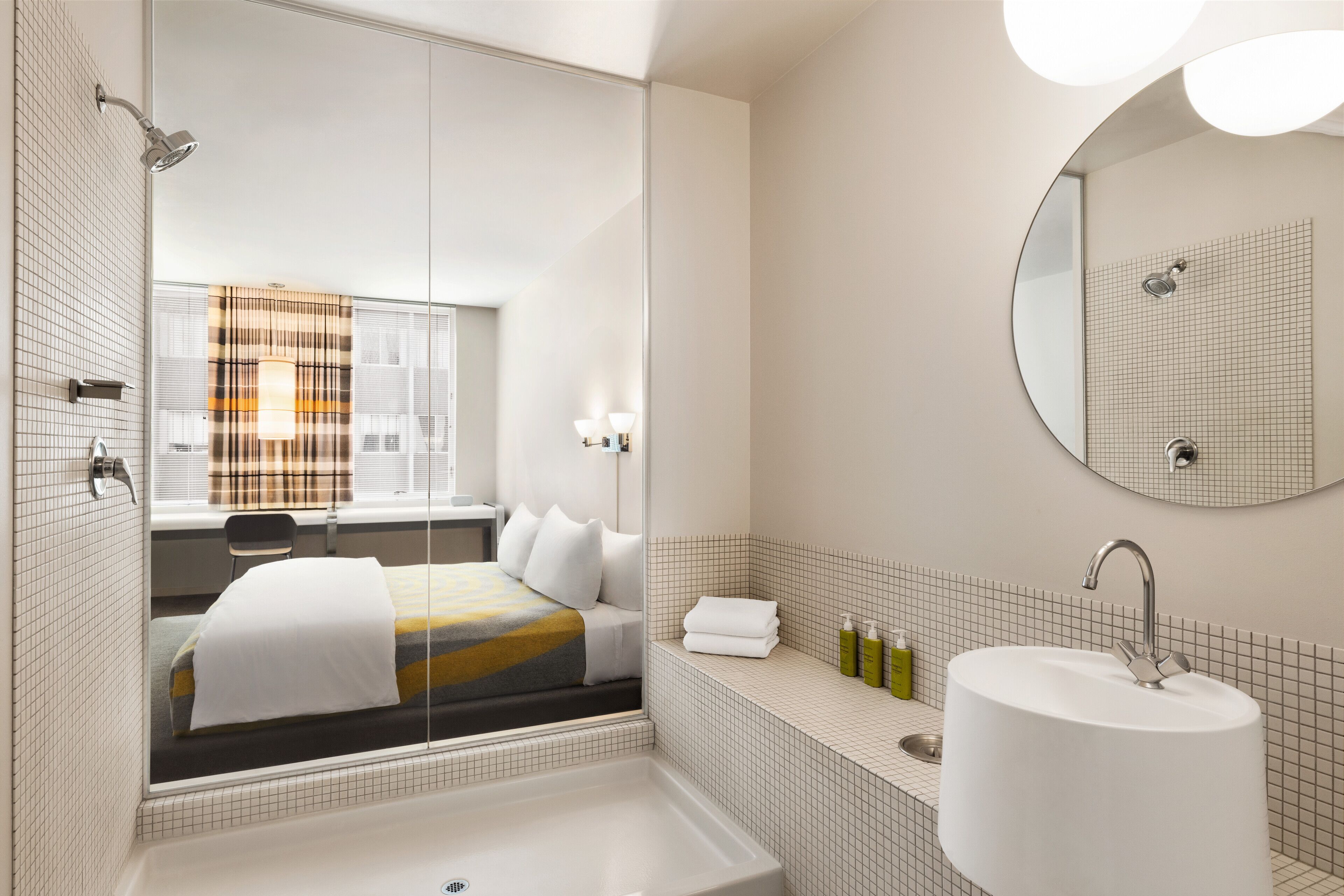 A modern bathroom with a large bathtub, a round mirror, and a window with a view of the city.