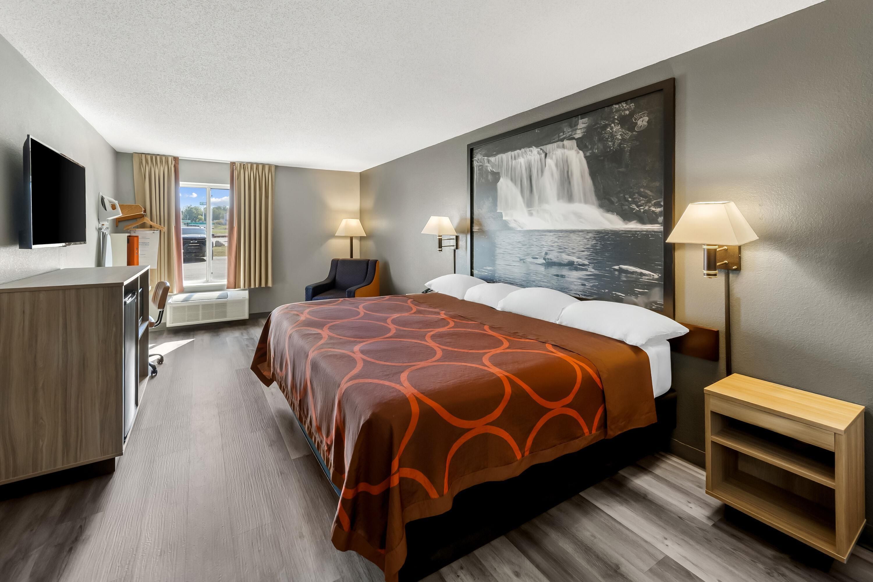 A hotel room with a bed, a desk, a chair, a TV, and a large window.