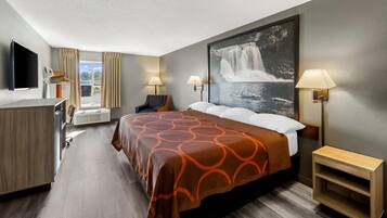 A hotel room with a bed, a desk, a chair, a TV, and a large window.