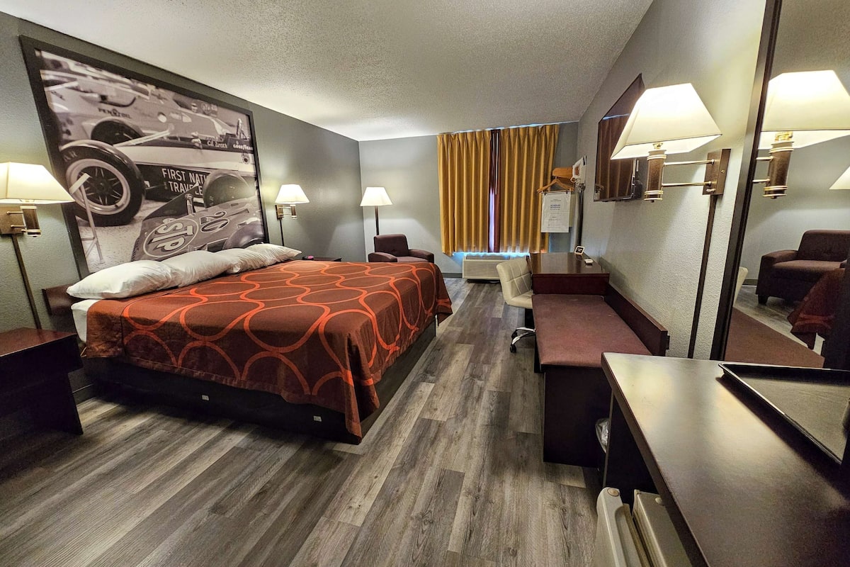 A hotel room with a bed, desk, chair, and a large mirror.