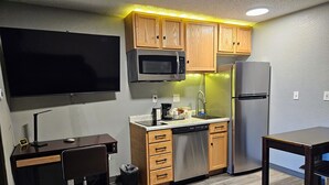 A compact kitchen with wooden cabinets, a microwave, a refrigerator, a sink, and a small dining table.