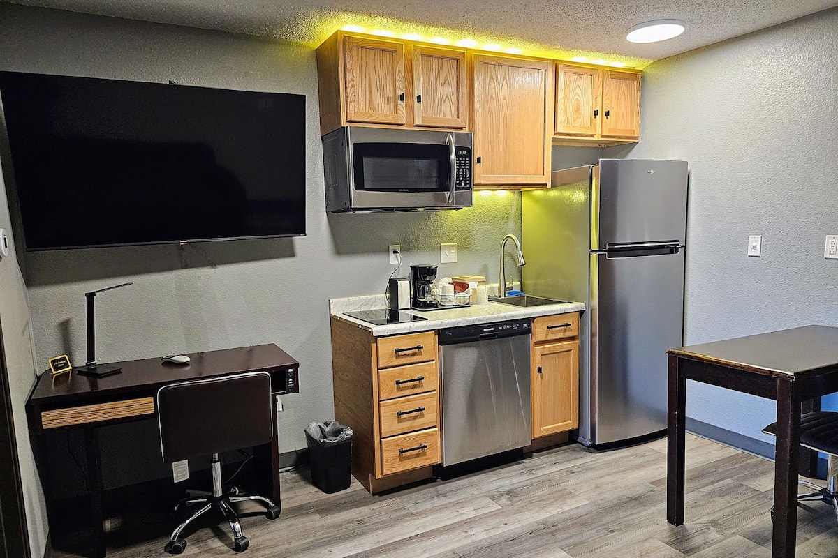 A compact kitchen with wooden cabinets, a microwave, a refrigerator, a sink, and a small dining table.