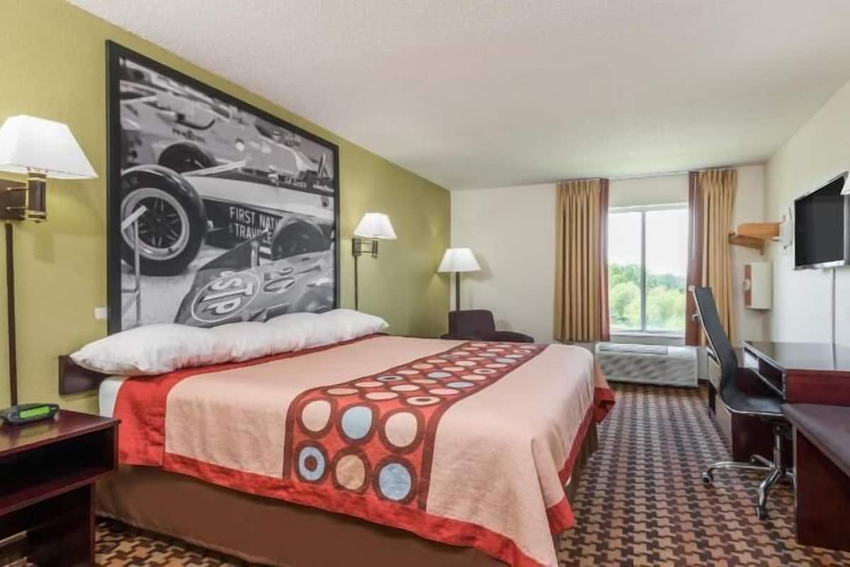 A hotel room with a bed, desk, chair, and a large window.