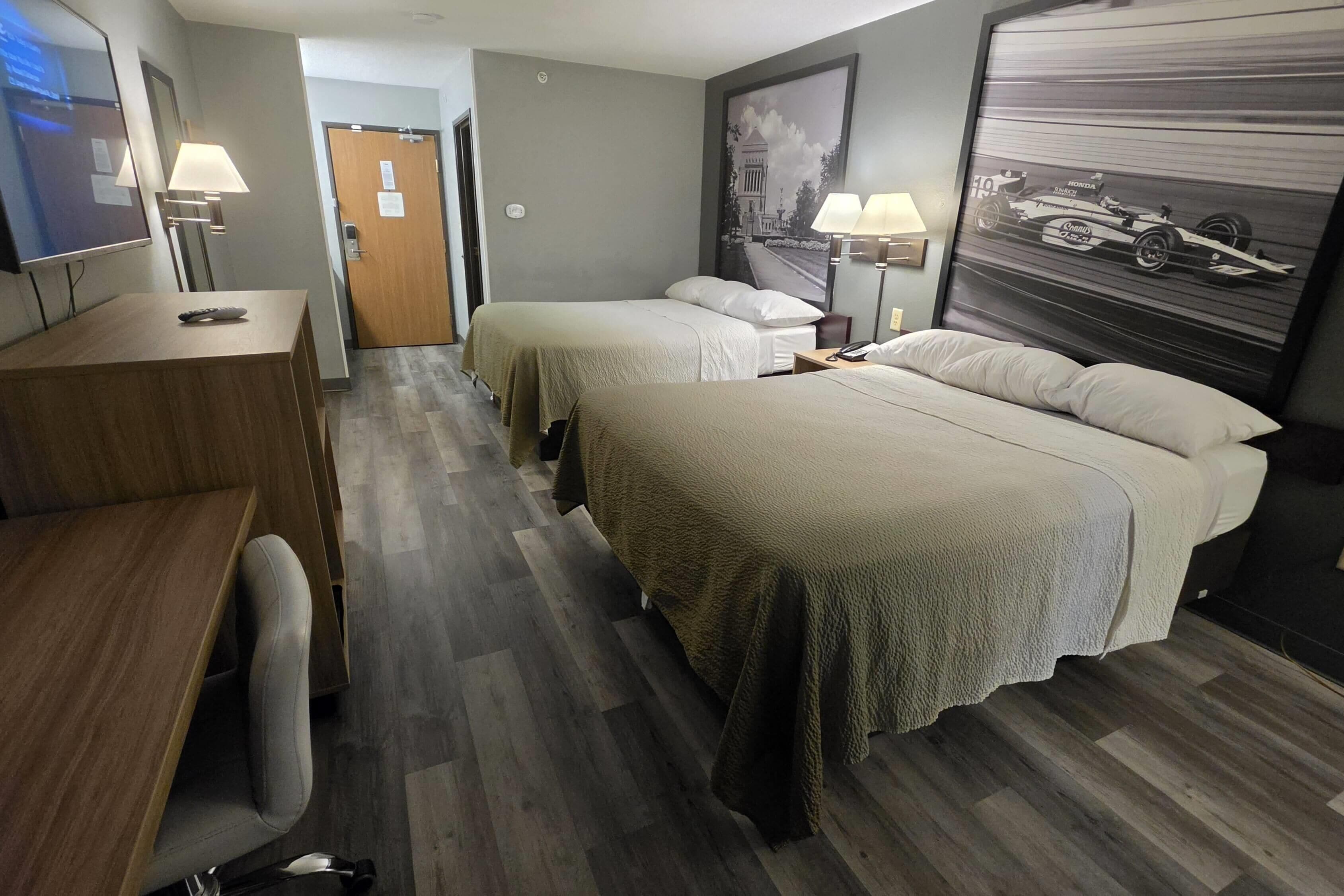 A hotel room with two beds, a desk, a chair, a TV, and a framed picture on the wall.