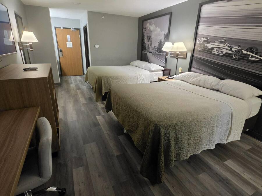 A hotel room with two beds, a desk, a chair, a TV, and a framed picture on the wall.