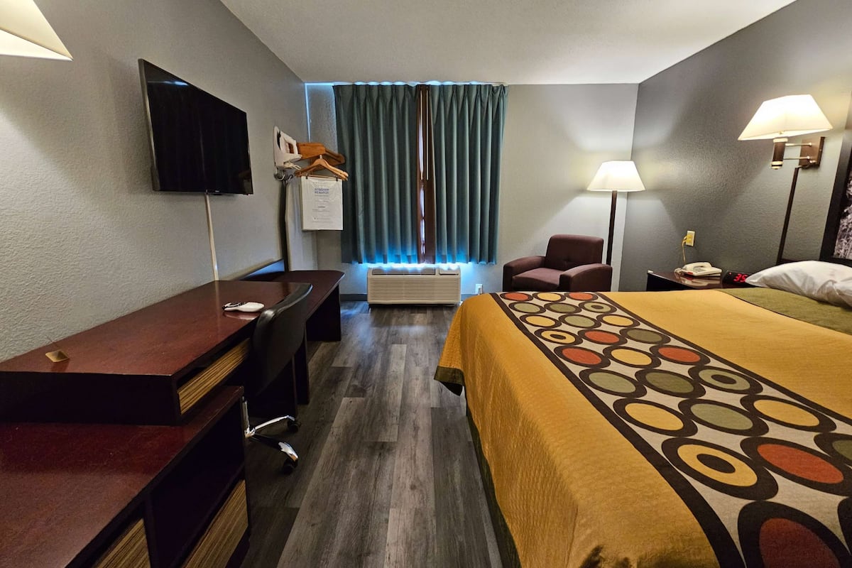 A hotel room with a desk, chair, bed, TV, air conditioning unit, and two bedside lamps.