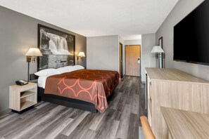 Habitación de hotel con cama, lámparas de noche, escritorio con teléfono, televisor grande de pared y cómoda de madera.