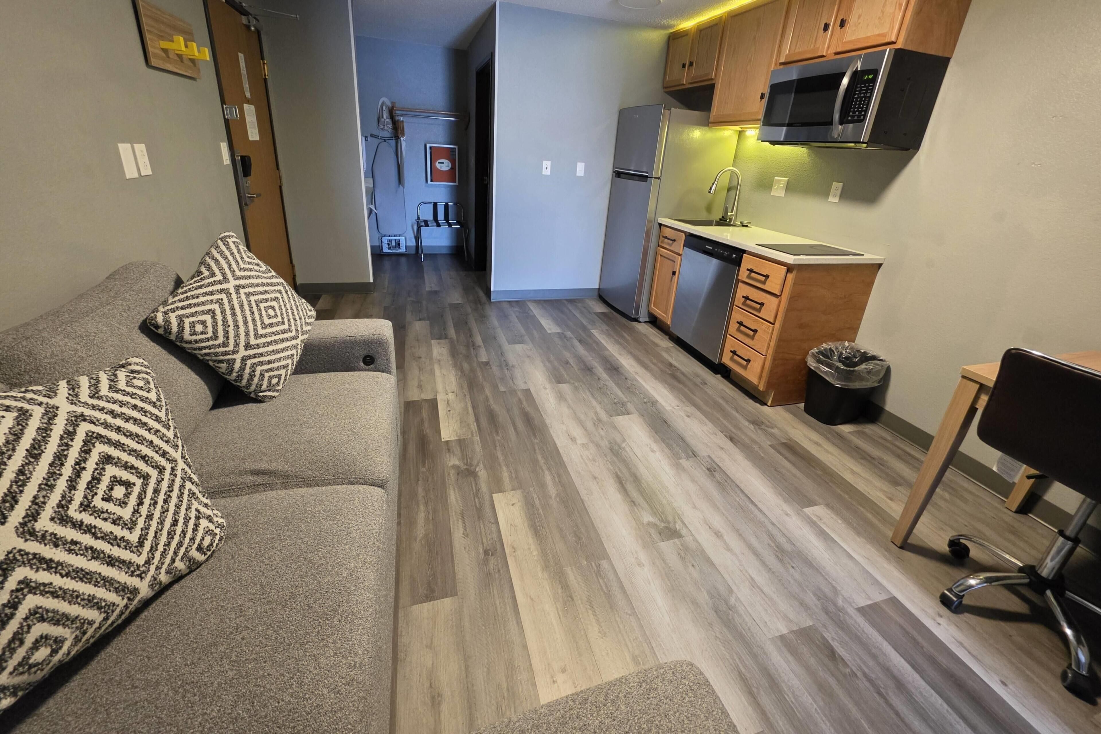 A compact living space with a kitchenette, a sofa with patterned cushions, and a chair.