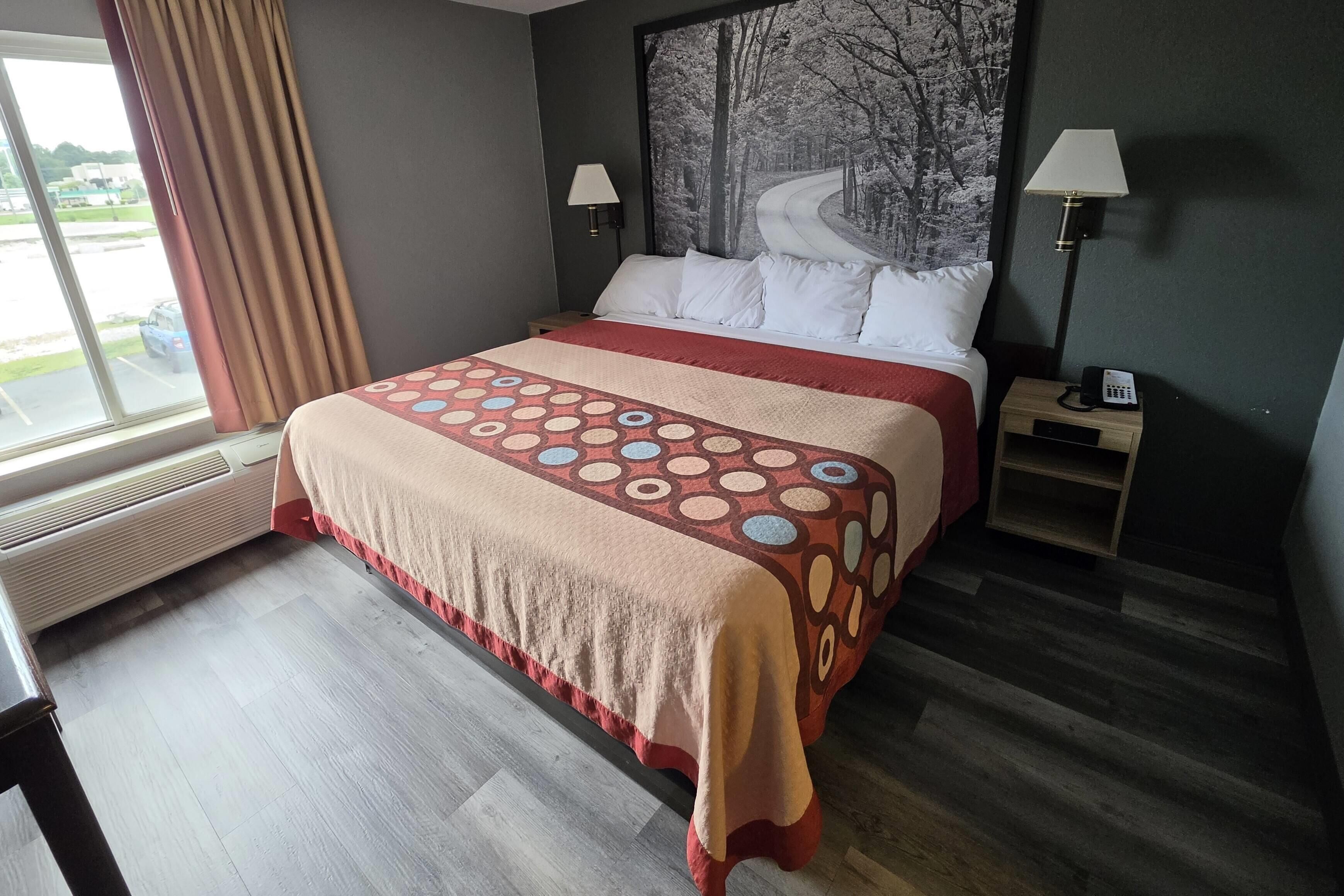 Une chambre d’hôtel avec un lit, une table de chevet, une lampe, un radiateur et une fenêtre avec des rideaux.