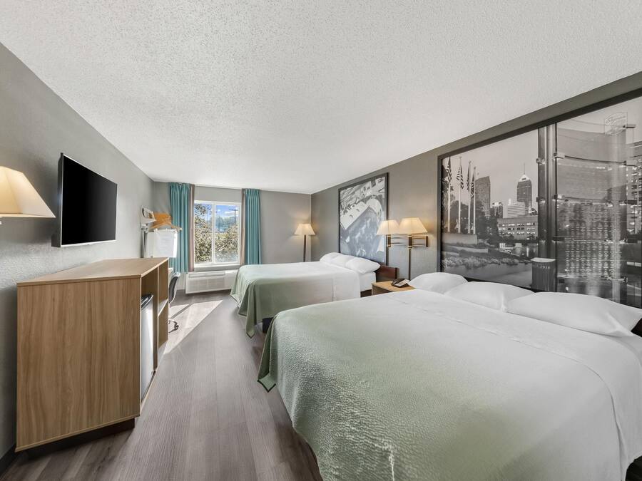 Habitación de hotel con dos camas, un escritorio, un televisor de pantalla plana y un ventanal con vista a la ciudad.