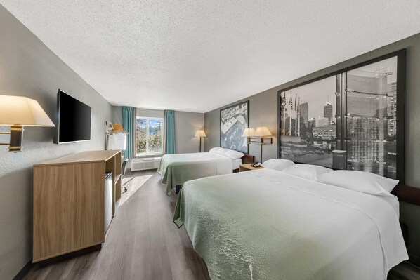 A hotel room with two beds, a desk, a flat-screen TV, and a large window with a cityscape view.