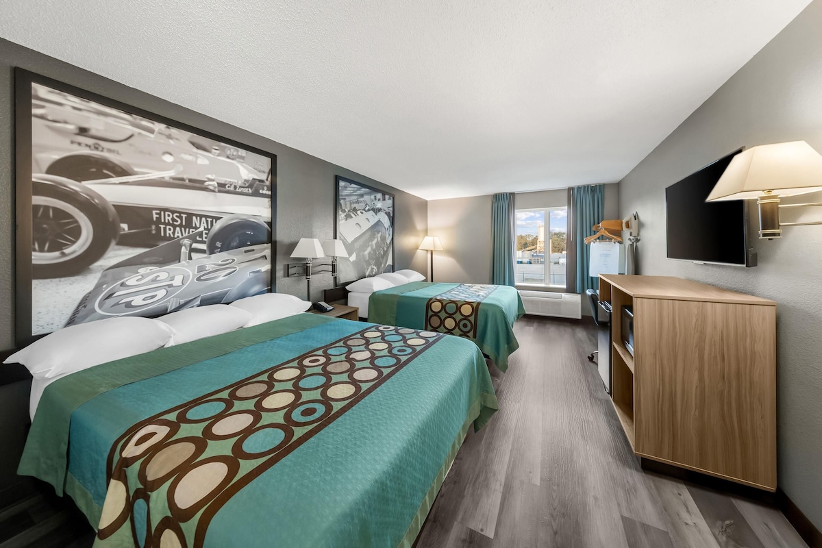 A hotel room with two beds, a desk, a TV, and a window with curtains.