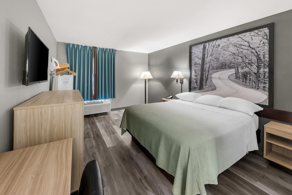 A hotel room with a bed, bedside table, lamp, and a large window with curtains.