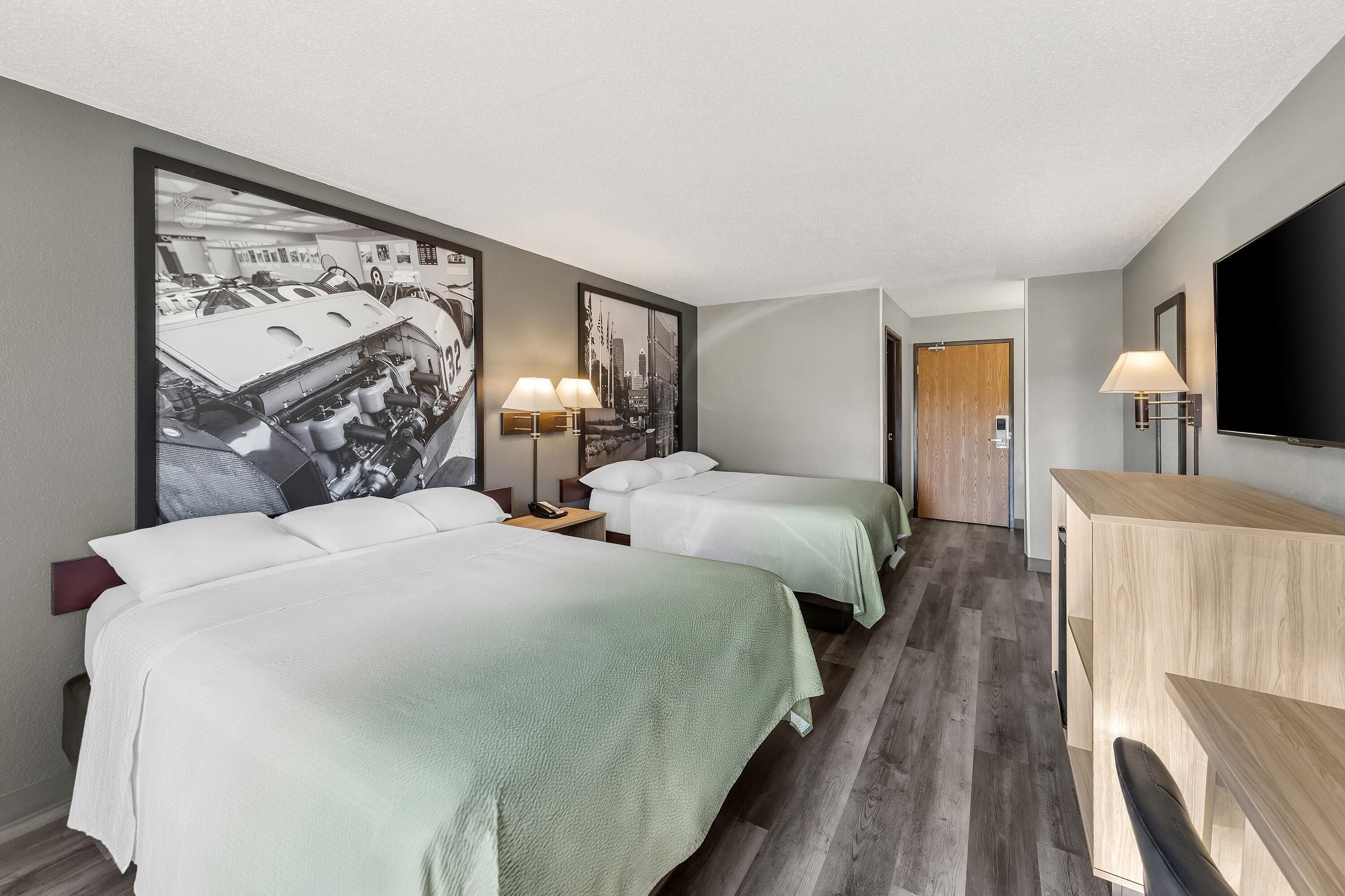 A hotel room with two beds, a desk, a TV, and a large wall art piece.