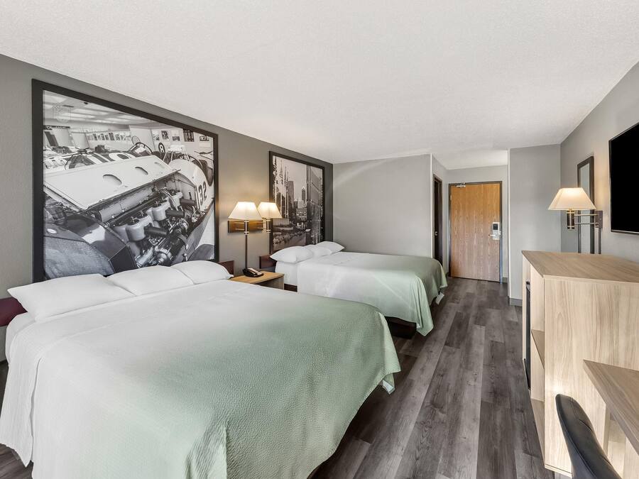 Habitación de hotel con dos camas, un escritorio, un televisor y una obra de arte grande en la pared.