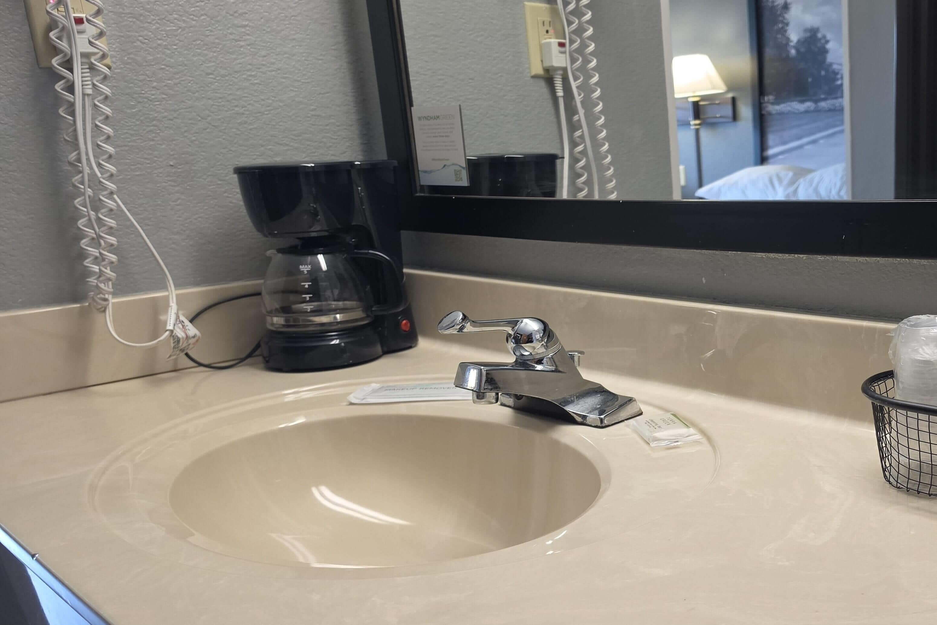 A hotel bathroom with a sink, a mirror, a coffee maker, and a power outlet.
