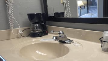 Un baño de hotel con lavamanos, espejo, cafetera y toma de corriente.