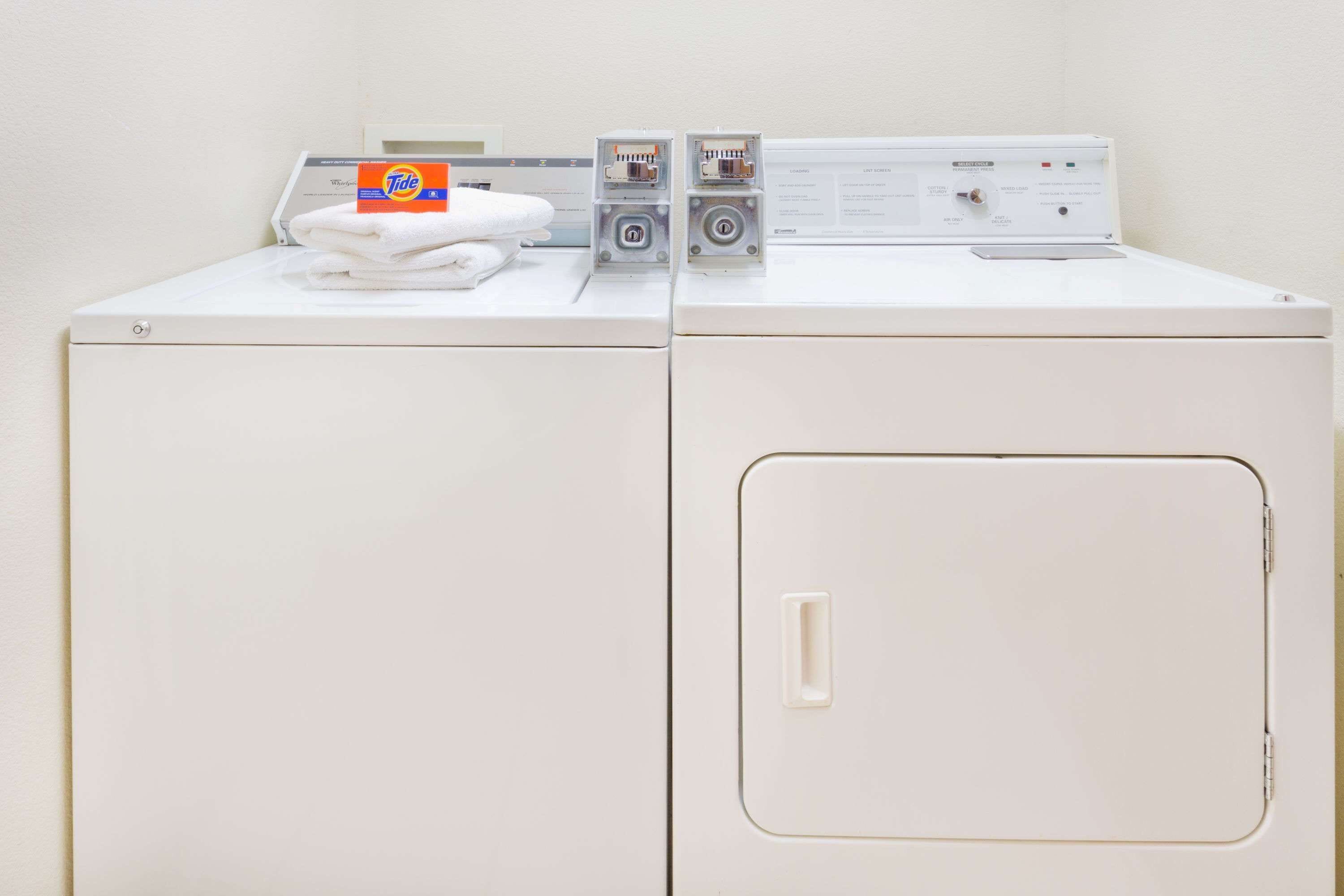 A front-loading white washing machine with a control panel, a Tide detergent box, and a folded white towel on top.