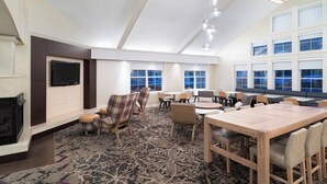 Une pièce spacieuse avec une cheminée, une grande table à manger, de nombreuses chaises et un téléviseur fixé au mur.