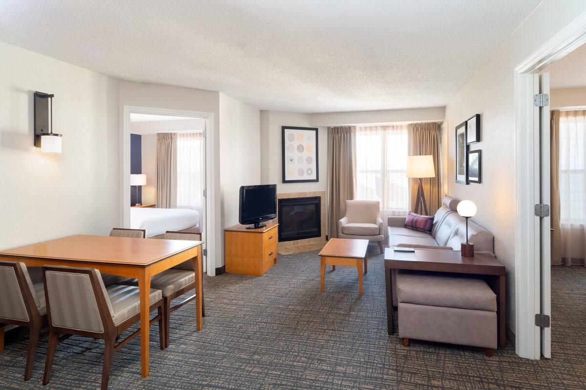 A hotel room with a dining table, chairs, a sofa, a TV, a fireplace, and a door.
