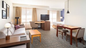 Une chambre d’hôtel comprenant un canapé, un bureau avec un ordinateur, une télévision, une table à manger avec des chaises et une lampe.