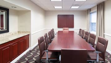 Un salón de conferencias con una larga mesa de madera, sillas de cuero marrón, una pizarra y un ventanal con cortinas.