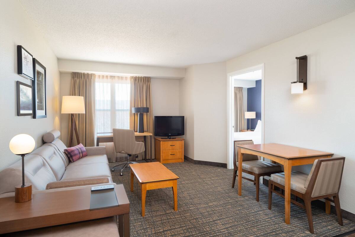 A hotel room with a sofa, a TV, a desk, and a chair.